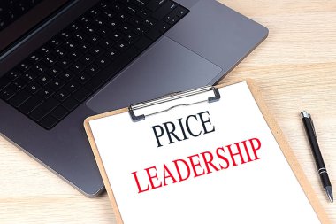 Price leadership concept with a clipboard, laptop, and pen on wooden desk .  clipart