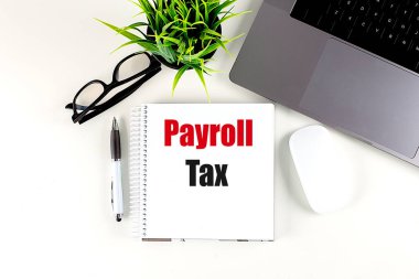 Payroll tax concept on a notebook with a laptop, glasses, pen, and plant on white desk. 