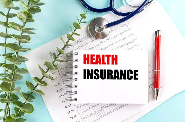 Steteskoplu bir not defterine sağlık sigortası metni, tıbbi çizelgeler ve açık mavi arka planda bir kalem. .
