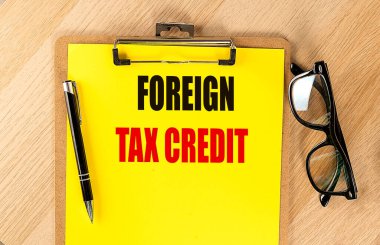 Sarı kağıda yabancı vergilerin yazılı olduğu not panosu, siyah kalem ve gözlüklerle ahşap bir masanın üzerine yerleştirilmiş. .