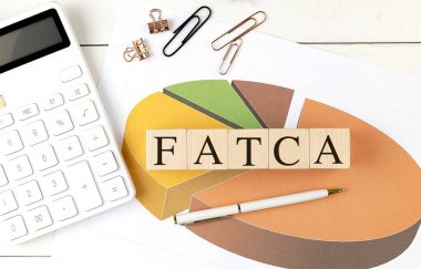 Tahta bloklar üzerinde FATCA metin pasta grafiği, hesap makinesi ve beyaz bir masa üzerinde kalem . 