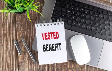 Vested benefit concept with notebook, laptop, pen, and plant on wooden desk .  clipart