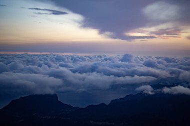 Gün batımında yumuşacık bulutlarla çevrili, gökyüzünde yumuşak pastel renkleri olan dağ zirvesinin dramatik manzarası. . 