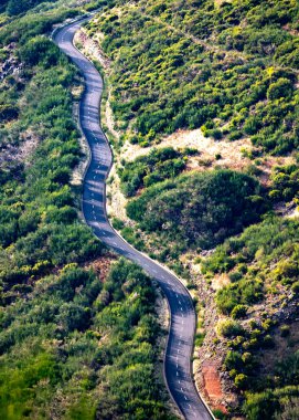 Sarmal asfalt yolu yemyeşil tepeleri ve engebeli araziyi kesiyor. . 