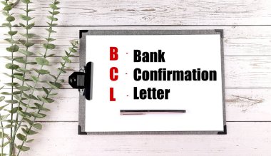 Board with the acronym BCL and its meaning bank confirmation letter on wooden table with green leaves and a pen .  clipart