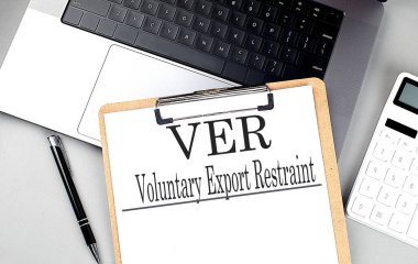 VER voluntary export restraint text on a clipboard with laptop, calculator, and pen on a gray desk .  clipart