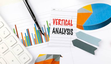 Renkli grafikler, klavye, kalem ve kağıt etiketlerle çevrili beyaz bir masanın üzerine yazılmış dikey analiz. . 