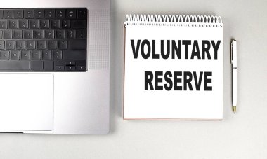 Dizüstü bilgisayarı ve gri arkaplanlı kalemi olan spiral bir defterde gönüllü yedek metin .