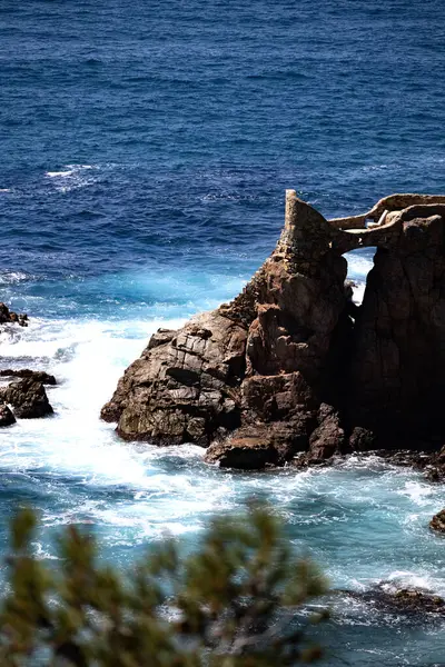 Taştan köprünün dikey görüntüsü dalgalı dalgalarla dalgalı turkuaz denizin üzerindeki kayalık kayalıkların üzerinde.. 