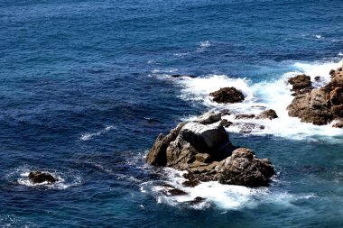 Dalgalar engebeli kıyı kayalarına çarpıyor canlı bir turkuaz ve derin mavi okyanus sularında. 