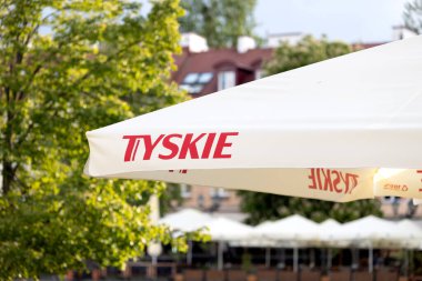 Bialystok, Polonya - 19 Mayıs 2025 Tyskie arka planda ağaçlar ve binalar bulunan açık bir oturma alanında beyaz veranda şemsiyesi markalaştırdı. 