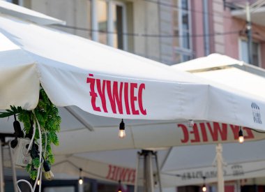 Bialystok, Poland- 27 Mayıs 2025: Zywiec markalı şemsiye asılı ampuller ve yeşillik ile şehir merkezindeki açık kafede . 