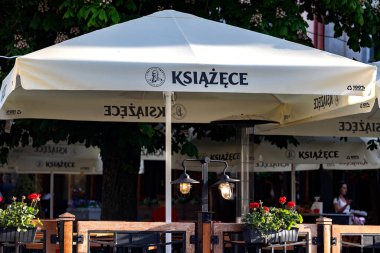 Bialystok, Poland- 27 Mayıs 2025: Ksiazece markalı şemsiyeler, çiçek kutuları ve dekoratif ışıklandırmalı açık hava yemek alanı. Yüksek kalite fotoğraf