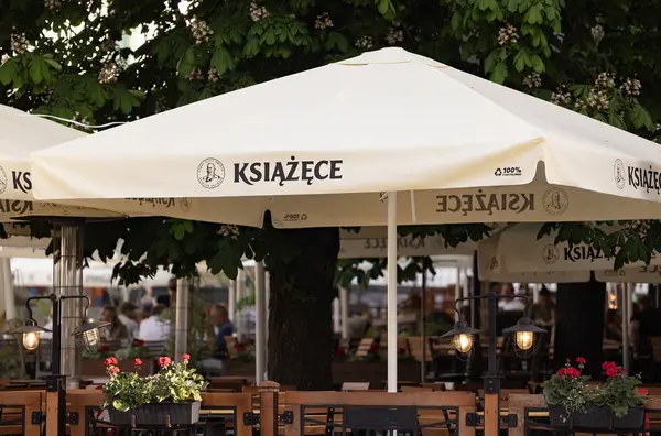 Bialystok, Poland- 27 Mayıs 2025: Ksiazece marka bira şemsiyeleri, ahşap masalar ve çiçek açan açık hava oturma alanı. 