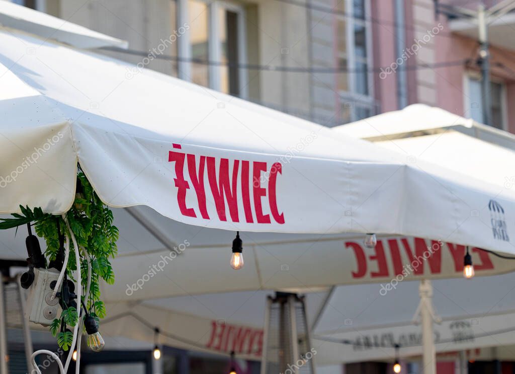 Bialystok,Poland- May 27 ,2025: Zywiec branded umbrella with hanging bulbs and greenery at outdoor cafe in city setting .