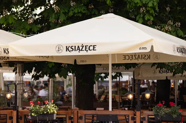 Bialystok, Poland- 27 Mayıs 2025: Ksiazece marka bira şemsiyeleri, ahşap masalar ve çiçek açan açık hava oturma alanı. 