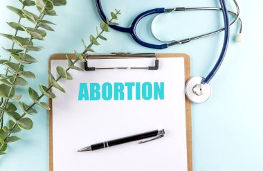 Steteskop, kalem ve yeşil yapraklı mavi arkaplan üzerinde metin kürtajı olan pano . 