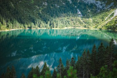 Ağaçları ve gökyüzünü yansıtan ormanlık bir kıyı şeridi olan turkuaz dağ gölü.. 
