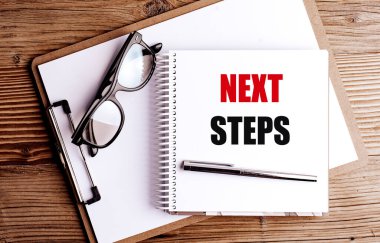 Not defterinde kelimeler var. Not panosundaki sonraki adımlar. Kalem ve gözlükler tahta arka planda. . 