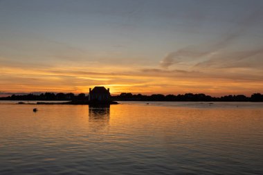 Gün batımında nehir kenarındaki ev