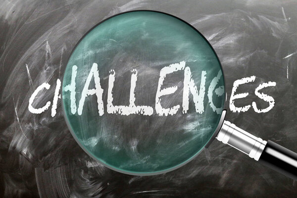 Challenges - learn, study and inspect it. Taking a closer look at challenges. A magnifying glass enlarging word 'challenges' written on a blackboard