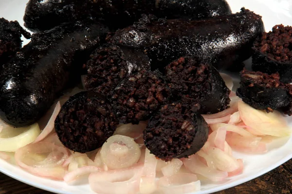 stock image Baked black pudding with pickled onions on a white plate. Sliced and fried blood sausage on a plate