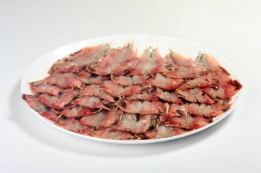 Birçok kişi beyaz bir arka planda küçük bir balığı bir tabakta açıp temizledi.