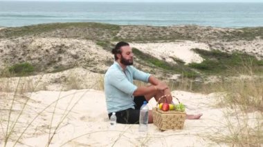 Sahilde piknik yaparken meyve yiyip su içen bir adam. Sağlık, sağlıklı beslenme ve açık hava aktivitesi kavramı.