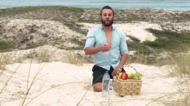 Sahilde piknik yaparken meyve yiyip su içen bir adam. Sağlık, sağlıklı beslenme ve açık hava aktivitesi kavramı.