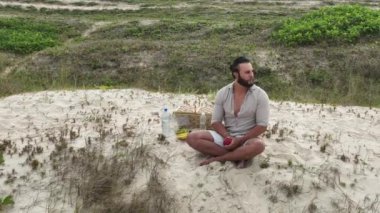Sahilde piknik yaparken meyve yiyip su içen bir adam. Sağlık, sağlıklı beslenme ve açık hava aktivitesi kavramı.
