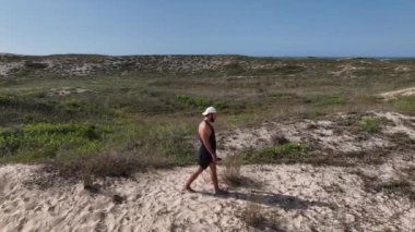 Sahildeki kum tepelerinde yürüyen ve koşan bir adam. Adamı takip eden İHA 'lı hava görüntüsü. Yukarıdan görüntü. Sağlık kavramı.