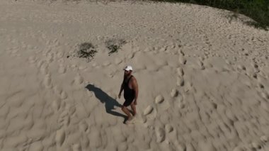 Sahildeki kum tepelerinde yürüyen ve koşan bir adam. Adamı takip eden İHA 'lı hava görüntüsü. Yukarıdan görüntü. Sağlık kavramı.