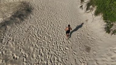 Sahildeki kum tepelerinde yürüyen ve koşan bir adam. Adamı takip eden İHA 'lı hava görüntüsü. Yukarıdan görüntü. Sağlık kavramı.
