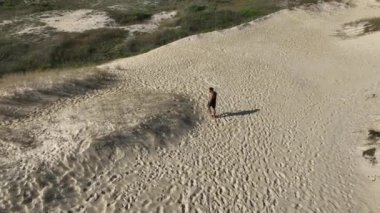 Sahildeki kum tepelerinde yürüyen ve koşan bir adam. Adamı takip eden İHA 'lı hava görüntüsü. Yukarıdan görüntü. Sağlık kavramı.