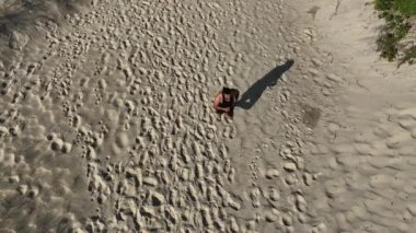 Sahildeki kum tepelerinde yürüyen ve koşan bir adam. Adamı takip eden İHA 'lı hava görüntüsü. Yukarıdan görüntü. Sağlık kavramı.