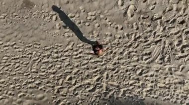 Sahildeki kum tepelerinde yürüyen ve koşan bir adam. Adamı takip eden İHA 'lı hava görüntüsü. Yukarıdan görüntü. Sağlık kavramı.