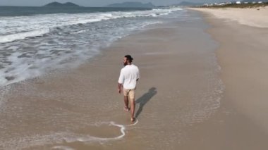 Güneşli bir sabahta sahilde koşmak ve yürümek. Kişiyi takip eden kameralı hava görüntüsü.