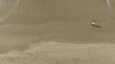 Güneşli bir sabahta sahilde koşmak ve yürümek. Kişiyi takip eden kameralı hava görüntüsü.