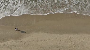 Güneşli bir sabahta sahilde koşmak ve yürümek. Kişiyi takip eden kameralı hava görüntüsü.