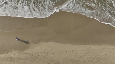 Güneşli bir sabahta sahilde koşmak ve yürümek. Kişiyi takip eden kameralı hava görüntüsü.