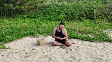 Kumsalda güneşli bir günde piknik yapan, yemek yiyen ve su içen bir adam. Açık hava konsepti. Hava görünümü.