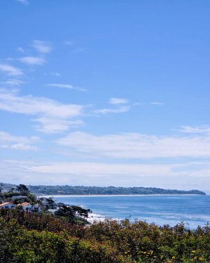 Huzurlu bir sahil manzarası, parlak mavi gökyüzünün altında geniş bir kıyı şeridini yakalıyor.. 
