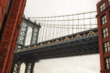 Manhattan Köprüsü 'nün çarpıcı bir resmi. Brooklyn' deki canlı DUMBO mahallesi tarafından çerçevelenmiş. Fotoğraf, köprünün neo-gotik kulelerini ve Doğu Nehri 'nin ve Manhattan ufuk çizgisinin nefes kesici manzarasını yakalıyor. Kullanım için mükemmel 