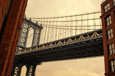 Manhattan Köprüsü 'nün çarpıcı bir resmi. Brooklyn' deki canlı DUMBO mahallesi tarafından çerçevelenmiş. Fotoğraf, köprünün neo-gotik kulelerini ve Doğu Nehri 'nin ve Manhattan ufuk çizgisinin nefes kesici manzarasını yakalıyor. Kullanım için mükemmel 