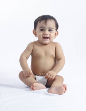 Bebek bezi takan sevimli çocuk, arka planda masum pozlar vererek yerde oturuyor, büyümeyi ve erken çocukluk dönüm noktalarını simgeliyor..