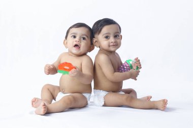 Beyaz stüdyoda yan yana oturan mutlu bebekler, oyuncaklarla oynaşan ifadeler, birlikteliği temsil eden ebeveynlik, çocuk bakımı ve aile yaşam tarzı..