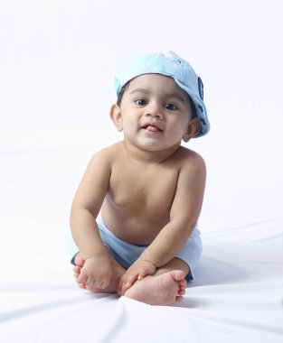 Yan şapkalı bebek bezi takan, beyaz stüdyoda oturan, eğlenceli, masumiyeti, aileyi ve erken çocukluk yaşam tarzını sembolize eden neşeli poz veren sevimli bir bebek..