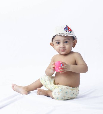 Bebek portresi stüdyo zemininde bebek bezi ve oyuncağıyla oturuyor, neşeli ifade, çocukluk oyunu, masumiyet, ebeveynlik ve aile kavramları için mükemmel..