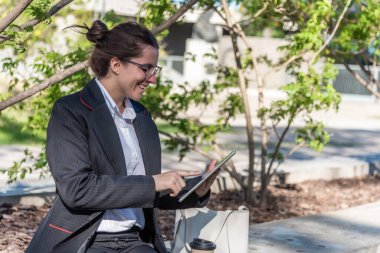 Female entrepreneur with glasses using digital tablet while sitting outdoors. Business and technology concept.