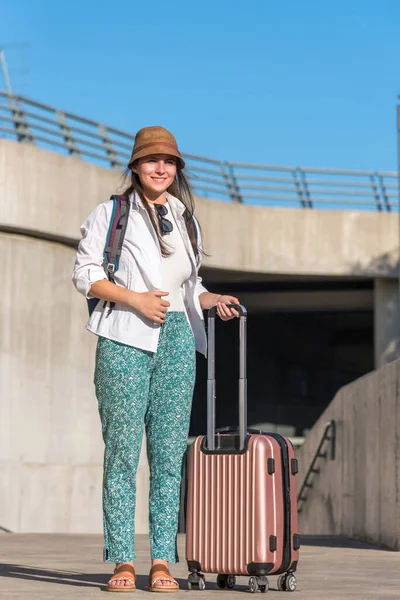 stock image Female traveler smiling while standing outdoors with a suitcase. Travel and tourism concept.